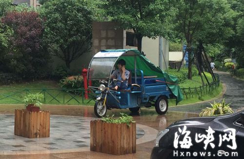 這名快遞哥騎行在小區(qū)通道內(nèi)，一邊接打手機，一邊還把腳架在車前欄桿上